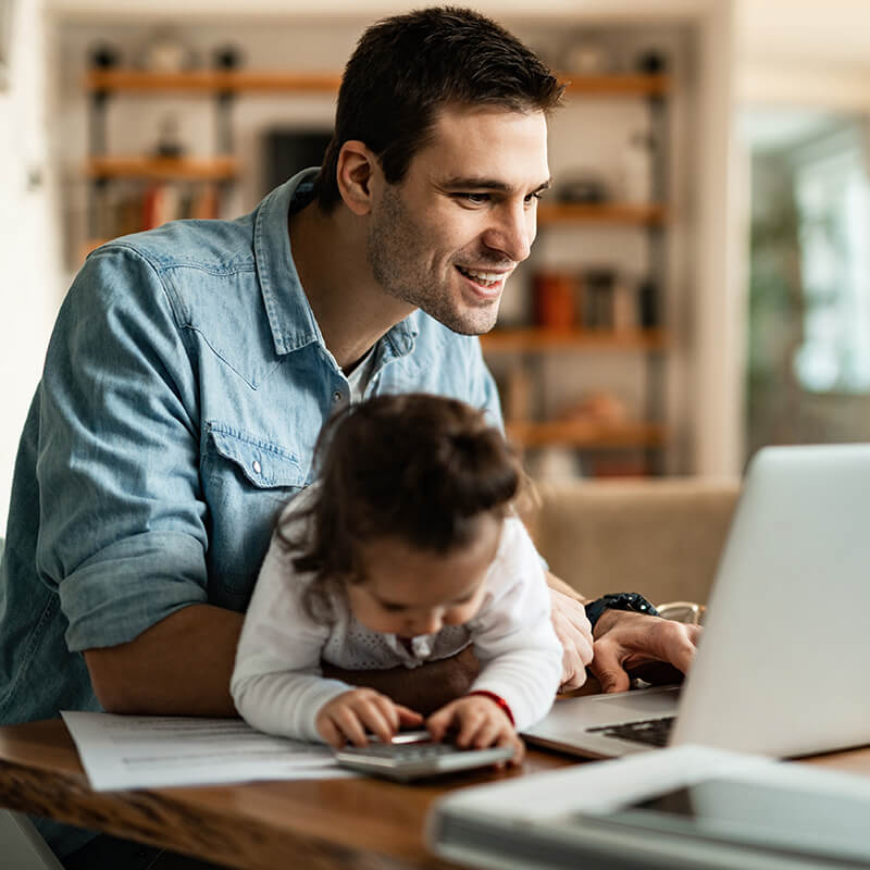 Young father holding his daughter while working on a laptop