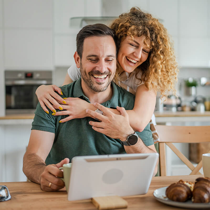 Husband and wife hugging while working on a tablet in their kitchen